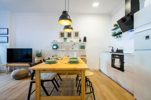 Apartamento moderno de planta abierta en Nerja con mesa comedor de madera, luces colgantes negras, cocina blanca, estantería y zona de TV