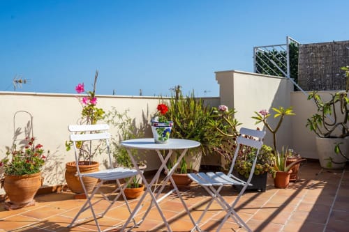 Terraza en azotea del apartamento de Nerja con muebles blancos, flores en macetas y vistas al mar bajo cielo azul despejado