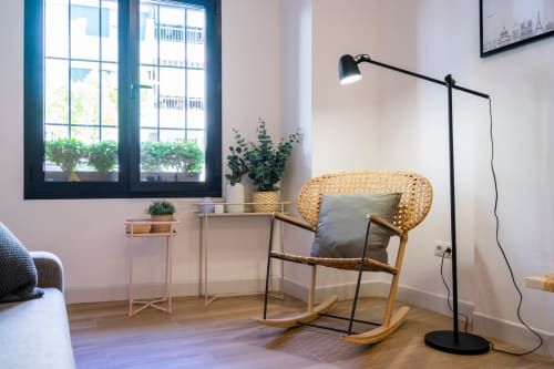 Interior moderno del apartamento en Nerja con sillón mecedor, luz natural de ventanas, plantas y lámpara de lectura