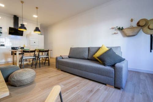 Moderno salón en Nerja con sofá gris, mesa de comedor, cocina y suelos de madera