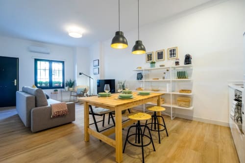 Moderno apartamento en Nerja con mesa de comedor de madera, taburetes amarillos, lámparas colgantes negras y salón con puertas azules