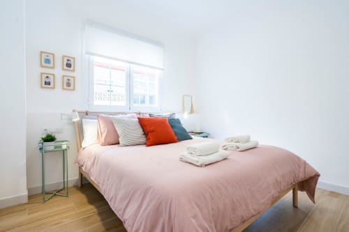 Dormitorio luminoso en Apartamentos Minaga Calle Chaparil, Nerja con ropa de cama rosa, almohadas coloridas, marco de cama de madera y