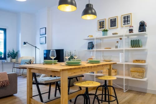 Comedor moderno en apartamento de Nerja con mesa de madera, taburetes amarillos, lámparas colgantes negras y estantería blanca