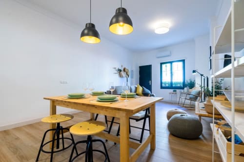 Comedor moderno en apartamento de Nerja con mesa de madera, taburetes amarillos, lámparas colgantes y vistas al mar por ventanas azules