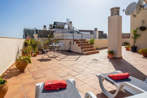 Soleada terraza en la azotea de Apartamentos Minaga en Nerja con tumbonas, plantas en macetas y vistas a la ciudad