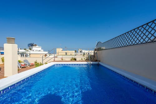 Piscina en la azotea de Apartamentos Minaga en Nerja con agua cristalina, tumbonas y vistas a la ciudad costera