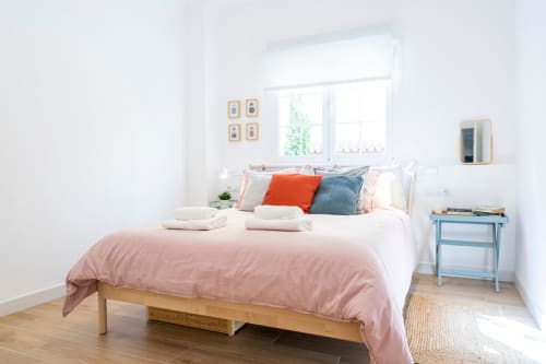 Dormitorio luminoso en apartamento Minaga, Nerja con cama queen, almohadas coloridas, mesilla de madera y luz natural