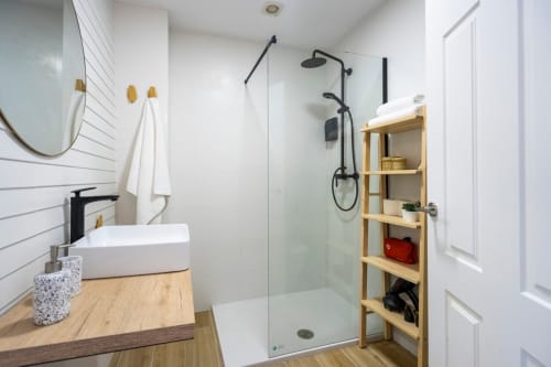Baño moderno en apartamento de Nerja con azulejos blancos tipo metro, accesorios negros, estantería de madera y ducha abierta