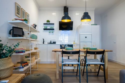 Moderna zona de cocina-comedor en apartamento de Nerja con mesa de madera, lámparas colgantes negras, muebles blancos y estanterías abiertas