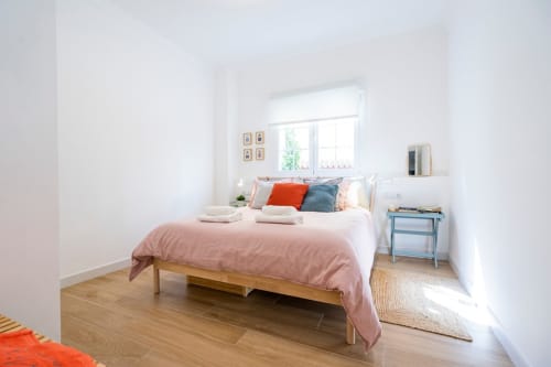 Dormitorio moderno y luminoso en Apartamentos Minaga Calle Chaparil, Nerja con ropa de cama rosa, suelo de madera y luz natural