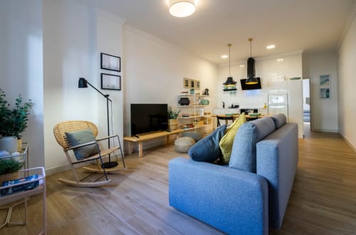 Moderno salón de apartamento en Nerja con sofá azul, suelos de madera, TV, cocina y mobiliario elegante
