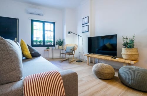 Apartamento moderno en Nerja con sala de estar, televisión, cómodos asientos y luz natural desde ventanas de marco azul