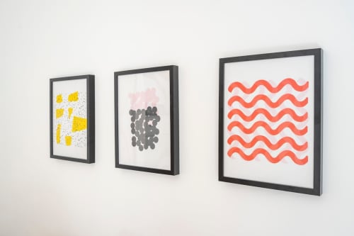 Tres obras de arte abstracto enmarcadas en apartamento moderno, con formas geométricas amarillas, círculos rosas y grises, y ondas rojas