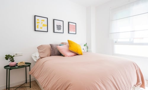 Dormitorio luminoso en Apartamentos Minaga de Nerja con ropa de cama rosa, almohada amarilla y arte moderno en la pared