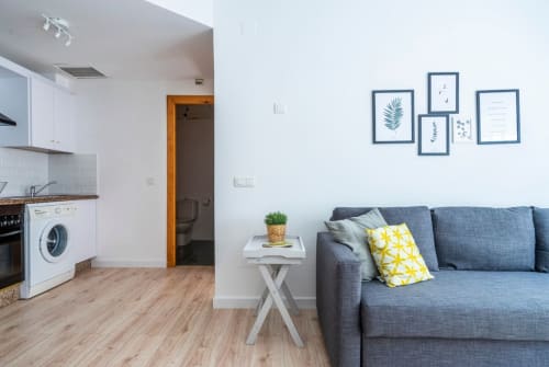 Moderno apartamento estudio en Nerja con cocina integrada, sofá azul y decoración de arte botánico en la pared