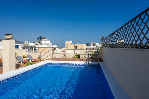 Piscina en azotea de Apartamentos Minaga en Nerja con vistas al mar, tumbonas y fondo azul mediterráneo