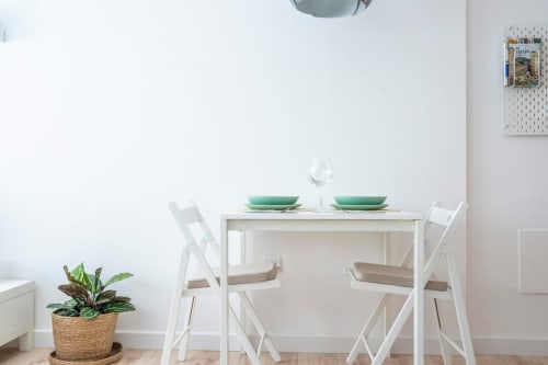Comedor luminoso con mesa y sillas blancas, platos verdes, planta en maceta y organizador de tablero en apartamento de Nerja