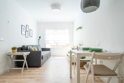 Moderno apartamento diáfano en Nerja con sofá gris, mesa de comedor, suelo de madera clara y paredes blanco brillante
