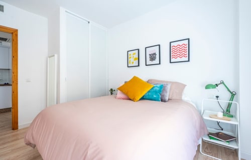 Luminoso dormitorio moderno en Apartamentos Minaga, Nerja, con ropa de cama rosa, almohadas coloridas, cuadros enmarcados y mobiliario blanco