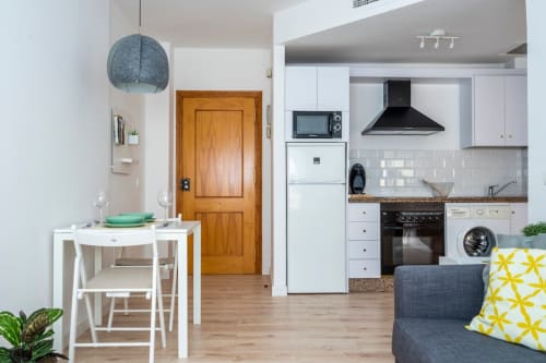 Moderno apartamento diáfano en Nerja con cocina blanca, comedor y sala de estar con puerta de madera y lámpara colgante azul