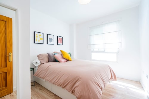 Dormitorio luminoso en apartamento de Nerja con ropa de cama rosa, almohadas coloridas y cuadros en la pared