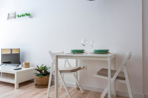 Zona de comedor moderna en apartamento de Nerja con mesa, sillas blancas, platos verdes y espacio de trabajo con plantas en macetas