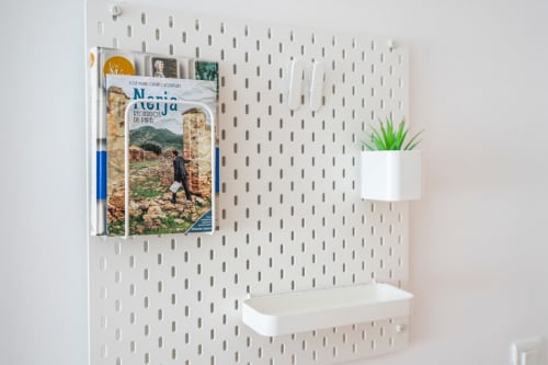 Pared de tablero blanco en apartamento de Nerja con revistero, maceta y repisa con guías de viajes