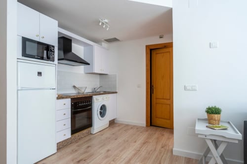 Cocina moderna en apartamento céntrico de Nerja con muebles blancos, electrodomésticos de acero inoxidable y suelo de madera