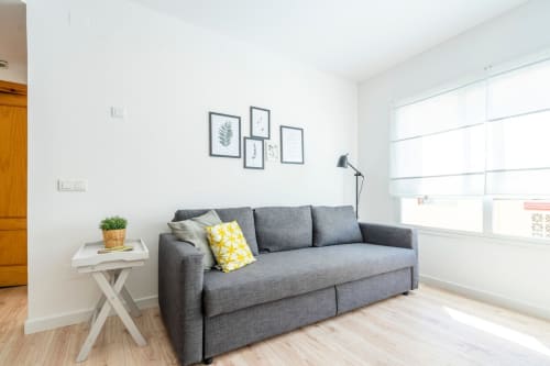 Salón moderno en apartamento de Nerja con sofá gris, cojín amarillo, mesita blanca y cuadros decorativos