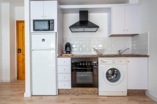 Cocina moderna en apartamento de Nerja con armarios blancos, encimeras de granito, campana negra, horno, microondas y lavadora