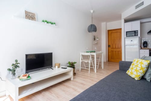 Moderno apartamento diáfano en Nerja con TV, zona de comedor, cocina y sofá gris con cojín amarillo