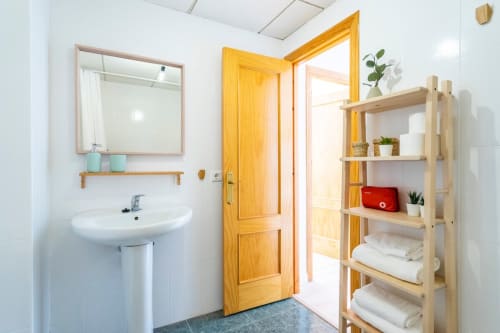 Luminoso baño en apartamento de Nerja con lavabo redondo, espejo, estanterías de madera y puerta amarilla hacia el pasillo
