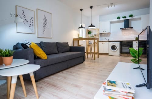 Moderno apartamento de planta abierta en Nerja con sofá oscuro, cocina, suelos de madera y decoración contemporánea.