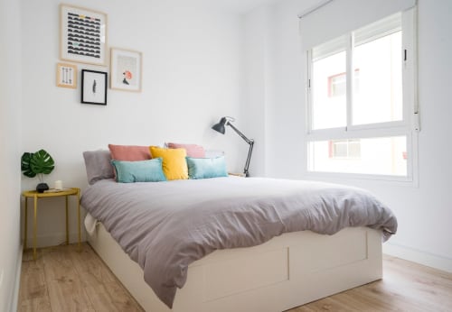 Dormitorio luminoso en apartamento de Nerja con cojines coloridos, mesita dorada y decoración moderna junto a la ventana