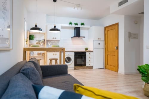 Cocina abierta y salón moderno en Apartamentos Minaga de Nerja con muebles de madera y lámparas colgantes negras