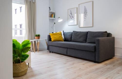 Sala de estar moderna en Nerja con sofá gris, cojín amarillo, suelos de madera y luz natural desde las ventanas