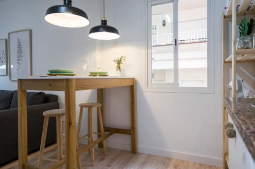 Moderna barra de cocina en apartamento céntrico de Nerja con mesa de madera, taburetes, lámparas colgantes y acceso a balcón