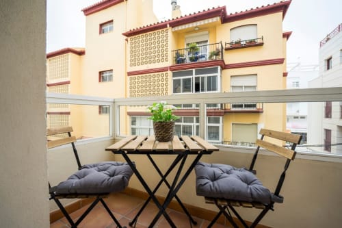 Terraza de balcón en Apartamentos Minaga en Nerja con sillas, mesa, planta en maceta y vistas del edificio amarillo