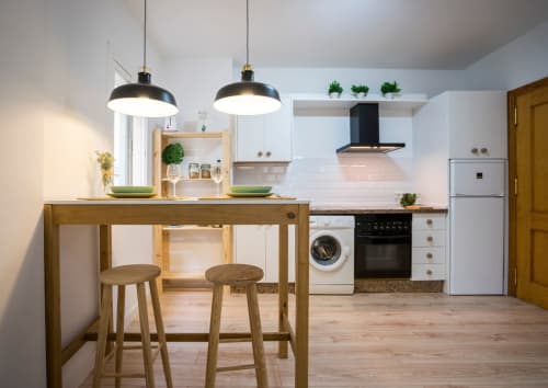 Cocina moderna en apartamento de Nerja con isla de madera, lámparas colgantes, electrodomésticos de acero inoxidable y gabinetes blancos.