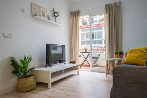 Salón moderno y luminoso en apartamento de Nerja con TV, sofá, plantas y balcón con vistas al pueblo
