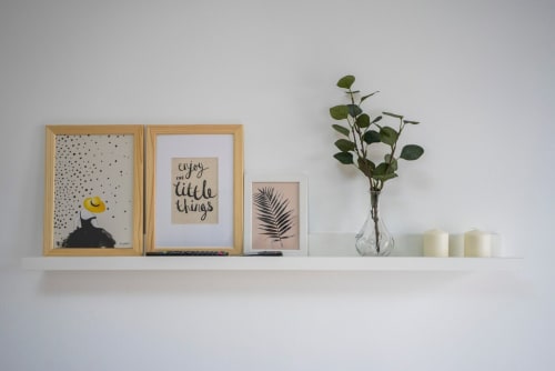 Decoración minimalista de estantería en apartamento de Nerja con cuadros, frases inspiradoras, estampado de helecho, flores frescas y velas