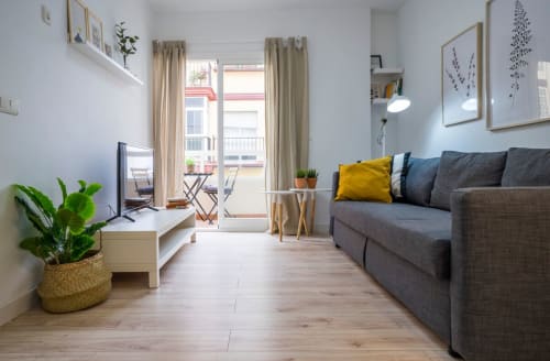 Moderna sala de estar en apartamento de Nerja con sofá gris, suelos de madera y acceso a balcón con vistas a la ciudad
