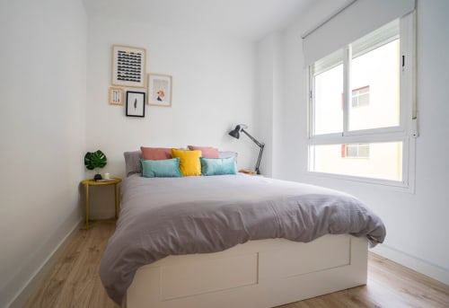 Dormitorio moderno en apartamento de Nerja con ropa de cama gris, almohadas coloridas, mesita con planta, cuadros enmarcados y