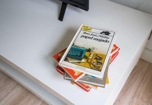 Pila de libros en estante blanco del apartamento de Nerja, incluyendo 'Papel mojado' de Juan José Millás