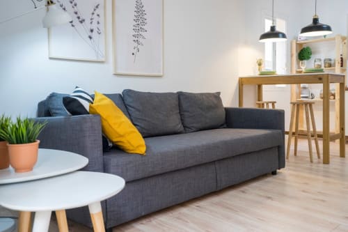 Sala moderna en apartamento de Nerja con sofá gris, cojín amarillo, estantería de madera y mesa redonda blanca