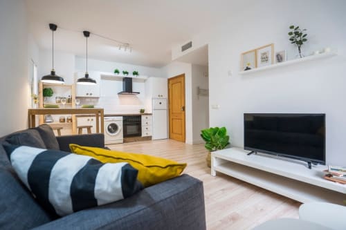 Moderno apartamento diáfano en Nerja con cocina americana, zona de estar, sofá gris, TV y detalles de madera