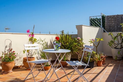 Soleada terraza en la azotea de Apartamentos Minaga en Nerja con plantas en macetas, mobiliario blanco y cielo azul despejado