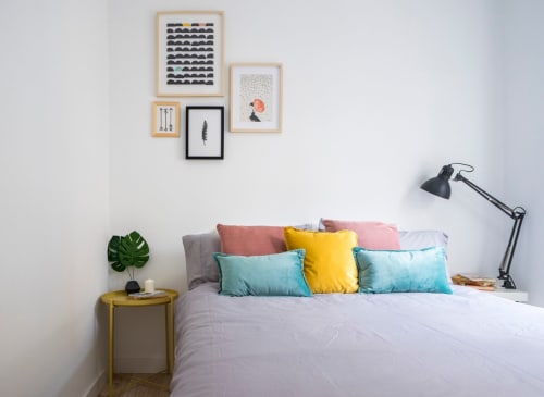 Dormitorio luminoso en apartamento de Nerja con cojines coloridos, arte moderno en la pared y mesita amarilla con planta