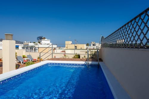 Piscina en la azotea de Apartamentos Minaga en Nerja con vistas a la ciudad y tumbonas