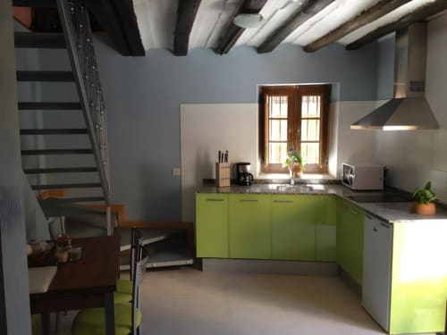 Cocina moderna con armarios verde lima, vigas vistas, ventana de madera y escalera en La Viña 1 de Casas Rurales La Viña